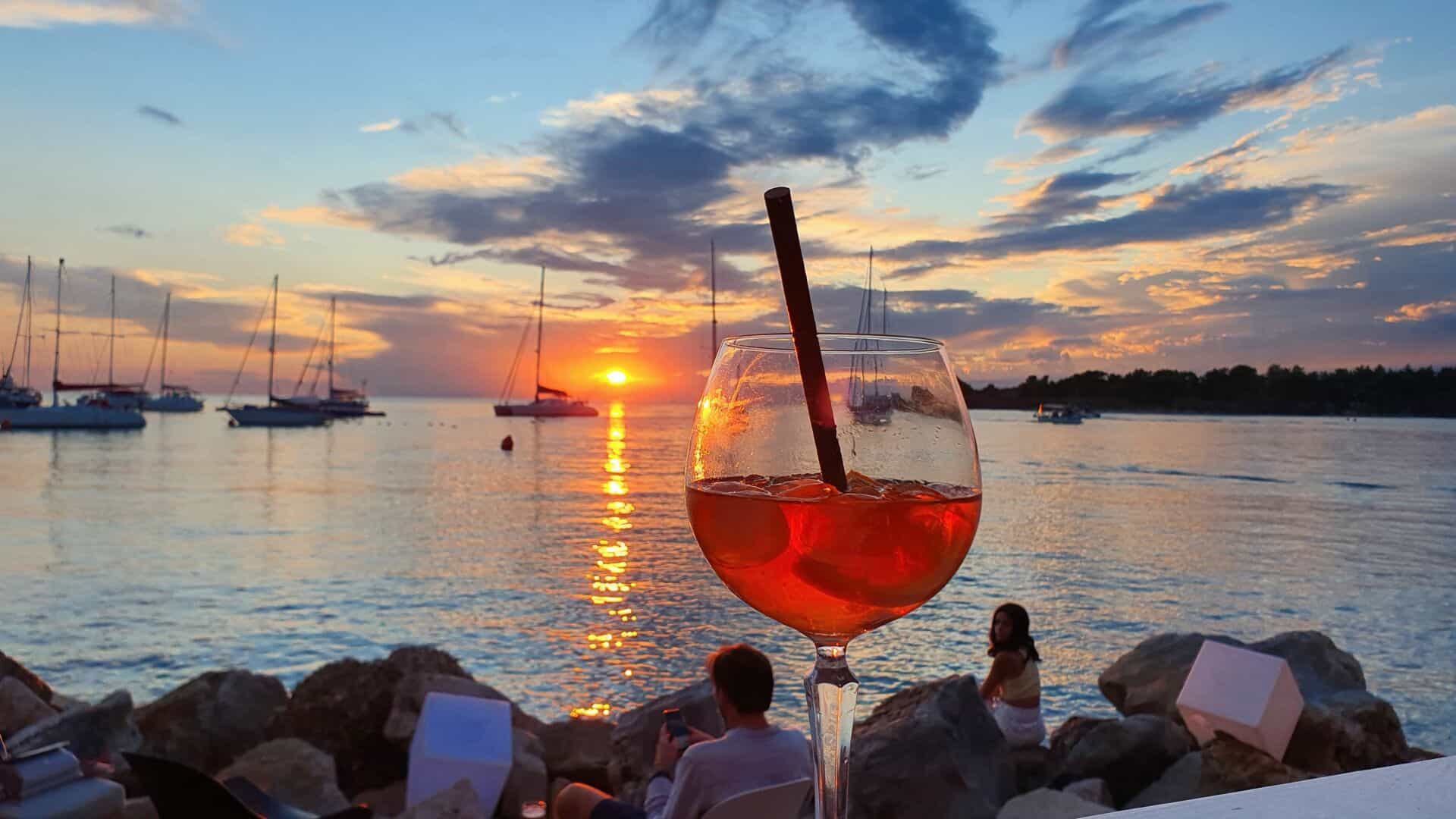 Zalazak sunca s koktelom na plaži i jedrilicama.